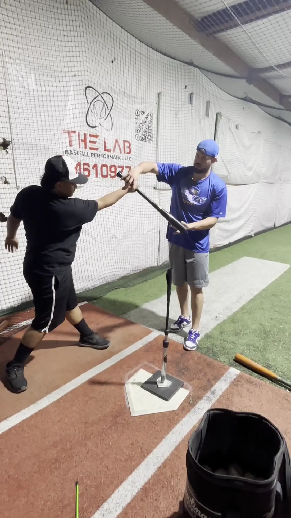 A coach working with a high school hitter at the tee inside The Lab